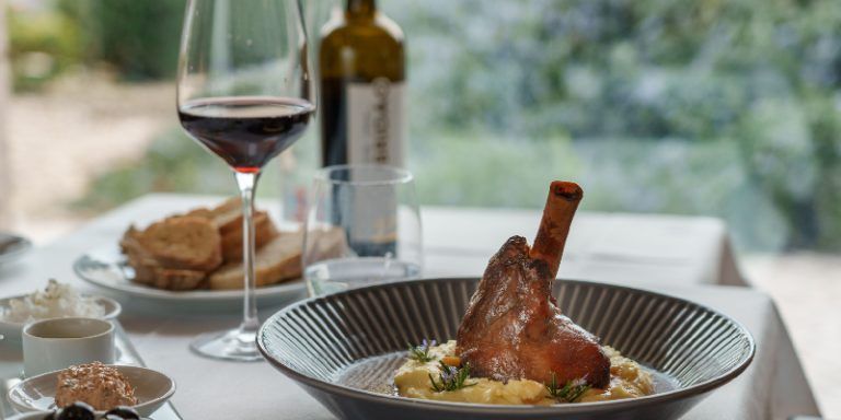 braised lamb shank on a plate next to a bottle of red wine