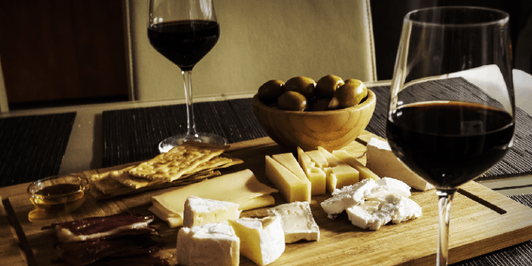 a glass of red wine next to a plate of Gouda And Brie cheese