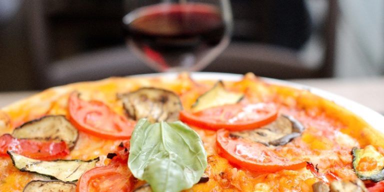 a pizza with tomatoes, cheese, and fresh basil and a glass of red wine