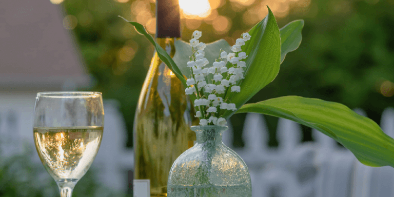 a glass of chardonnay white wine next to a flower on a table