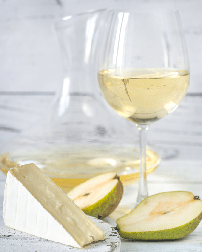 a glass of chardonnay wine next to a piece of brie cheese and pears