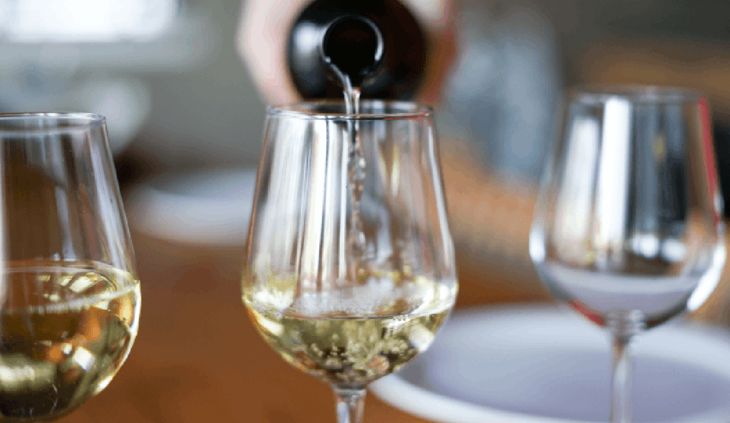 a bottle of chardonnay poured into a glass, next to another glass of white wine